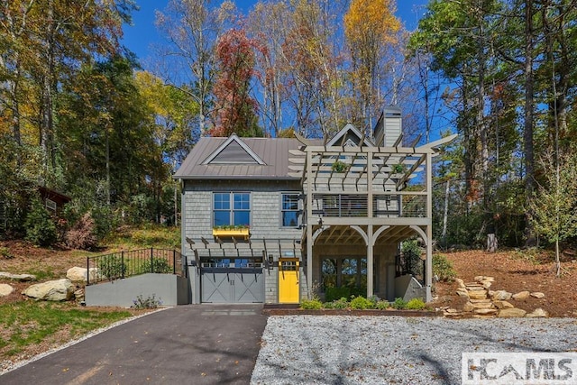 traditional home with asphalt driveway, an attached garage, a standing seam roof, a chimney, and metal roof