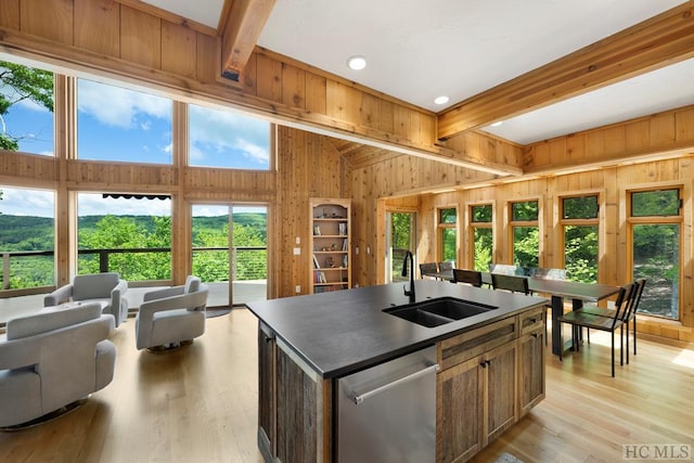 kitchen featuring sink, light hardwood / wood-style flooring, an island with sink, stainless steel dishwasher, and beamed ceiling