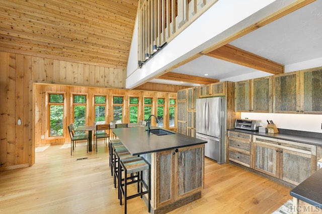 kitchen with stainless steel refrigerator, sink, a kitchen bar, a center island with sink, and light wood-type flooring