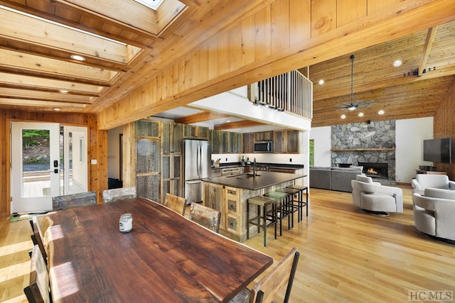 dining room featuring a towering ceiling, wooden walls, a fireplace, a skylight, and light wood-type flooring