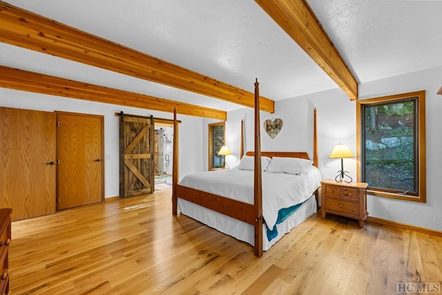 bedroom featuring beamed ceiling, a barn door, and light wood-type flooring