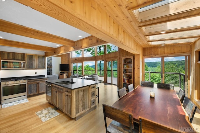 kitchen featuring a skylight, sink, a kitchen island with sink, stainless steel appliances, and beam ceiling