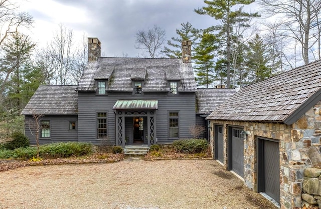 view of front of property featuring stone siding, a chimney, an attached garage, and driveway