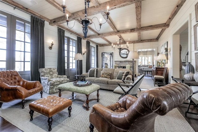 living room with a stone fireplace, beamed ceiling, wood finished floors, and an inviting chandelier