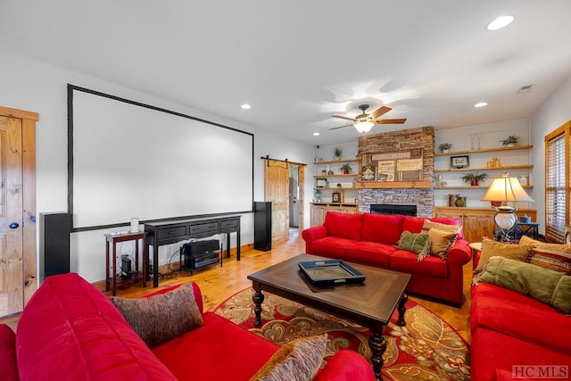 home theater featuring light hardwood / wood-style flooring, ceiling fan, a barn door, and a stone fireplace