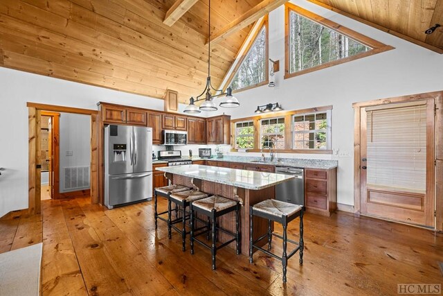 kitchen with appliances with stainless steel finishes, light stone countertops, decorative light fixtures, a kitchen island, and sink