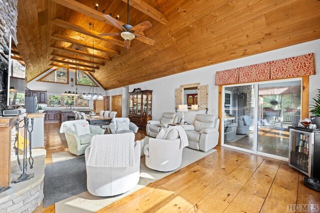 living room featuring ceiling fan with notable chandelier, light hardwood / wood-style floors, wooden ceiling, high vaulted ceiling, and beam ceiling