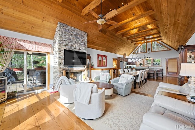 living room featuring vaulted ceiling with beams, a stone fireplace, light hardwood / wood-style floors, ceiling fan, and wooden ceiling