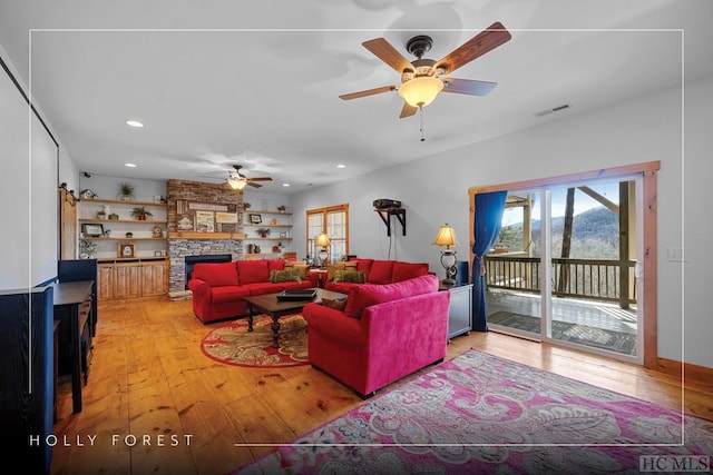 living room with hardwood / wood-style floors, ceiling fan, and a stone fireplace