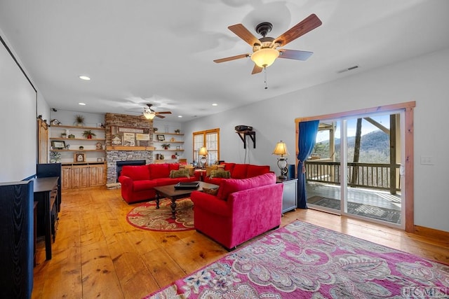 living room featuring a fireplace, ceiling fan, and light hardwood / wood-style floors