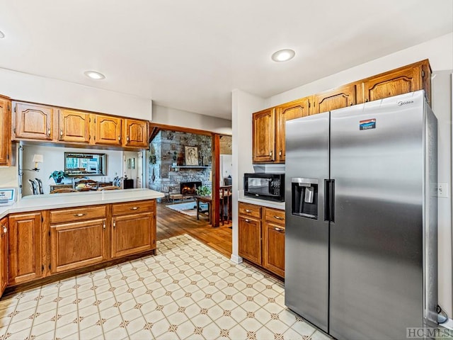 kitchen featuring a stone fireplace, kitchen peninsula, and stainless steel fridge with ice dispenser