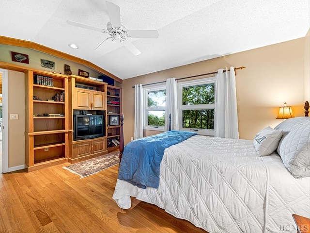 bedroom featuring a textured ceiling, vaulted ceiling, light hardwood / wood-style floors, and ceiling fan