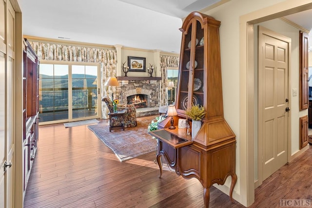 living room featuring hardwood / wood-style flooring, crown molding, a mountain view, and a stone fireplace