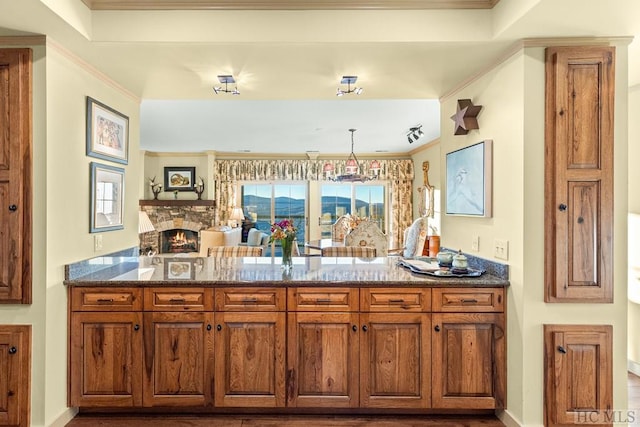 kitchen featuring ornamental molding, a stone fireplace, pendant lighting, and dark stone countertops