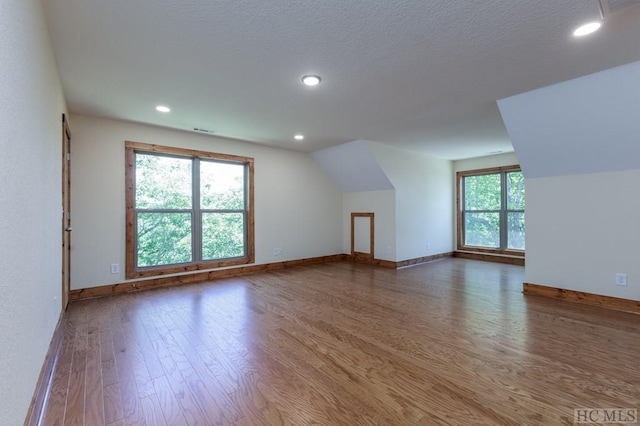 additional living space featuring dark wood-type flooring, plenty of natural light, and vaulted ceiling