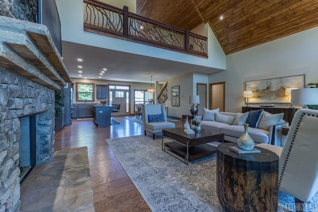 living room featuring a stone fireplace, dark wood-type flooring, wooden ceiling, and high vaulted ceiling