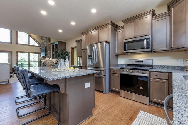 kitchen with a kitchen island, a breakfast bar, light stone counters, stainless steel appliances, and light hardwood / wood-style flooring