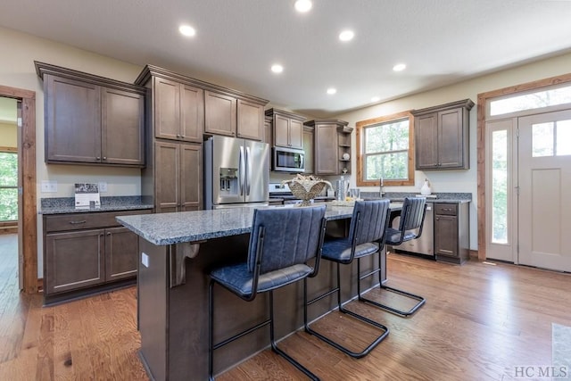 kitchen with a breakfast bar area, appliances with stainless steel finishes, light stone countertops, an island with sink, and light wood-type flooring