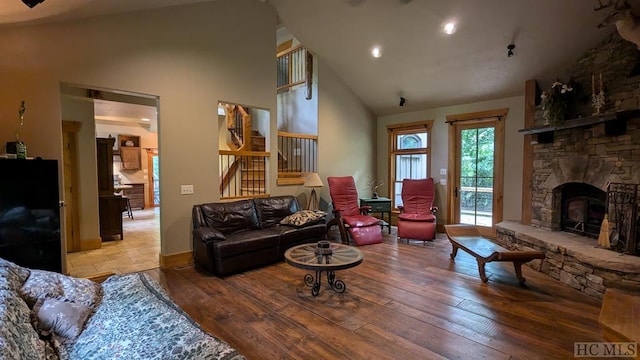 living room featuring wood-type flooring, a stone fireplace, and high vaulted ceiling