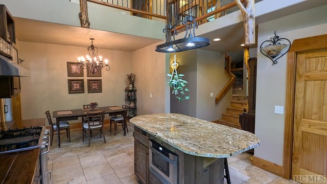 kitchen with a towering ceiling, pendant lighting, stainless steel gas stove, a center island, and an inviting chandelier