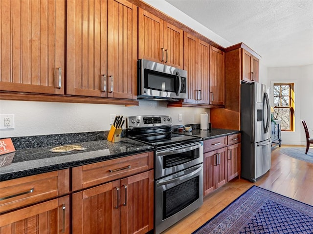 130 Cross Vine Dr, Tuckasegee, NC 28783 - kitchen with appliances with stainless steel finishes, light wood-type flooring, brown cabinets, and dark stone counters