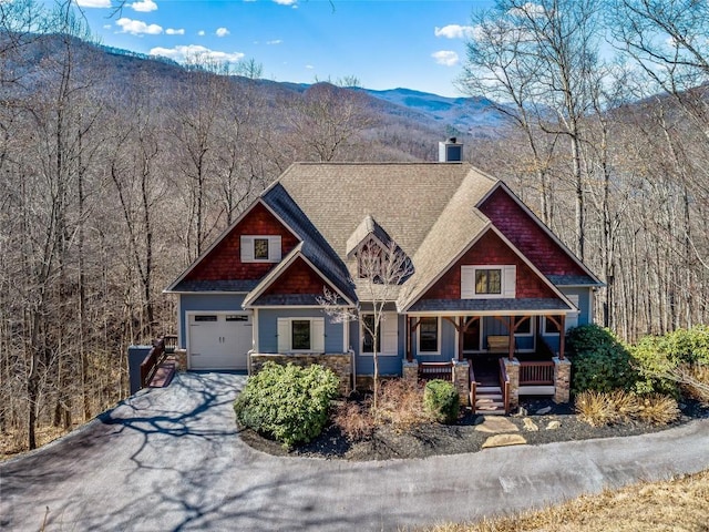 craftsman-style house with a garage, a view of trees, aphalt driveway, a mountain view, and a porch