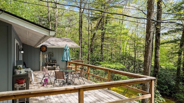 wooden terrace with outdoor dining space and a view of trees