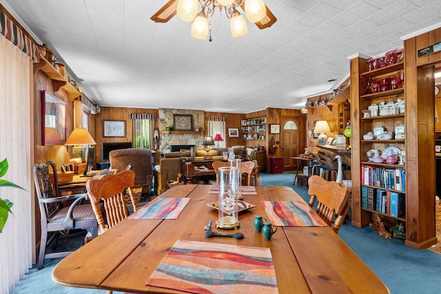 dining space featuring ceiling fan, carpet floors, wood walls, and a stone fireplace