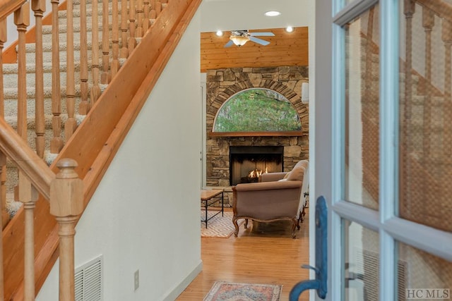 stairs with hardwood / wood-style floors, a stone fireplace, and ceiling fan