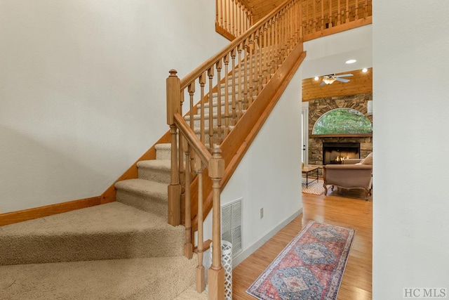 staircase featuring hardwood / wood-style flooring, a fireplace, and ceiling fan