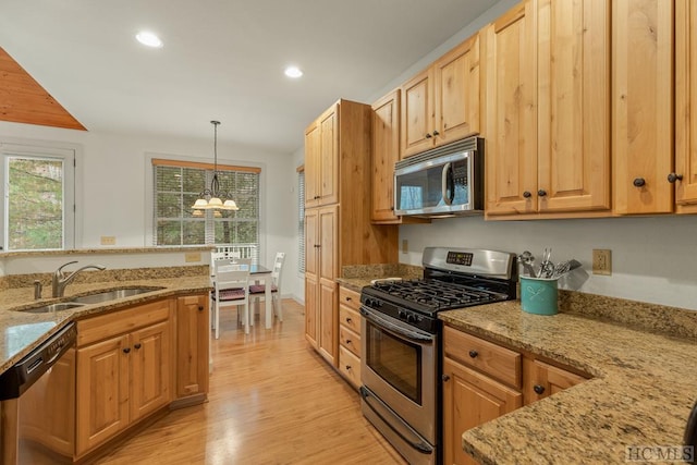 kitchen with sink, hanging light fixtures, appliances with stainless steel finishes, light stone countertops, and light hardwood / wood-style floors