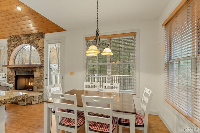 dining space featuring an inviting chandelier, a fireplace, light wood-type flooring, and wooden ceiling