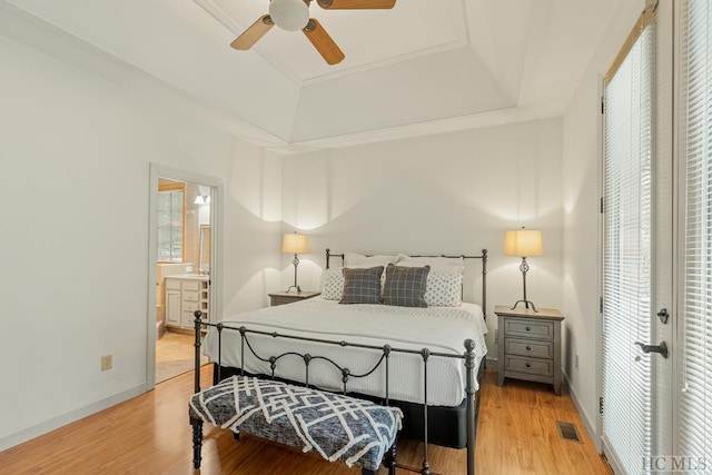 bedroom with ceiling fan, connected bathroom, a tray ceiling, french doors, and light wood-type flooring