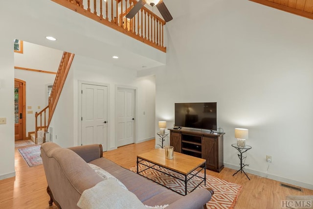 living room featuring ceiling fan, a towering ceiling, and light hardwood / wood-style floors