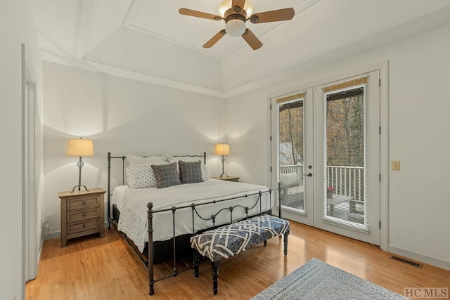 bedroom featuring ceiling fan, access to exterior, light hardwood / wood-style floors, a raised ceiling, and french doors