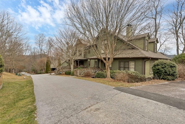 view of front of property with a porch, a chimney, aphalt driveway, and roof with shingles