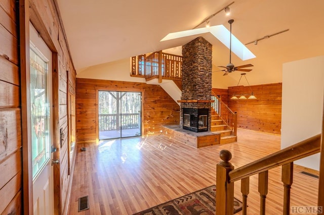 unfurnished living room featuring hardwood / wood-style flooring, rail lighting, vaulted ceiling with skylight, and wood walls