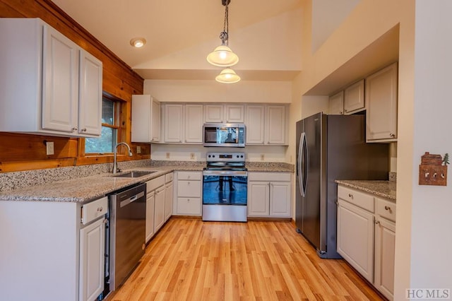 kitchen featuring vaulted ceiling, appliances with stainless steel finishes, sink, white cabinets, and hanging light fixtures