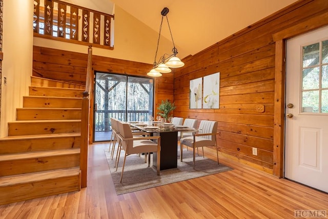 dining area with high vaulted ceiling, light wood-type flooring, and wooden walls