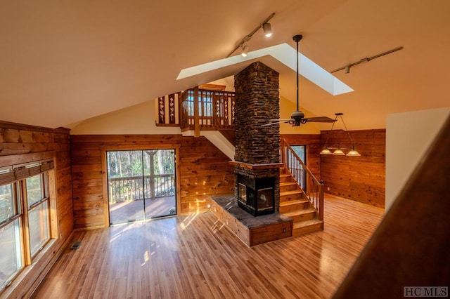 living room featuring rail lighting, wooden walls, lofted ceiling with skylight, and ceiling fan