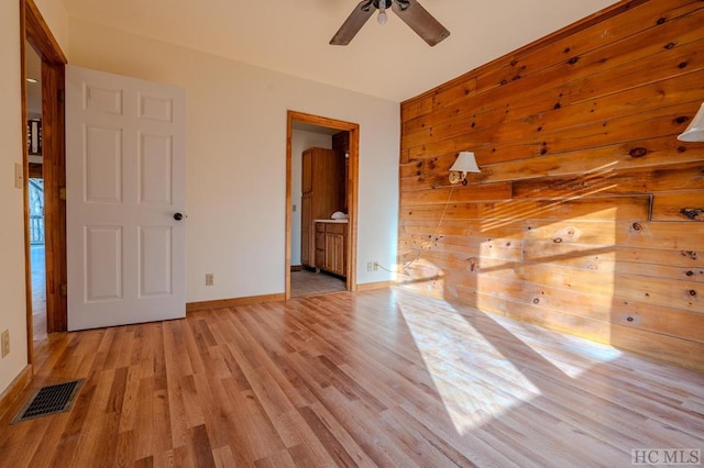 empty room featuring ceiling fan, wooden walls, and light hardwood / wood-style flooring