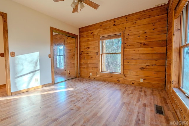 spare room with ceiling fan, wooden walls, and light hardwood / wood-style floors