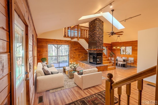 living room featuring rail lighting, a stone fireplace, a skylight, wooden walls, and hardwood / wood-style flooring