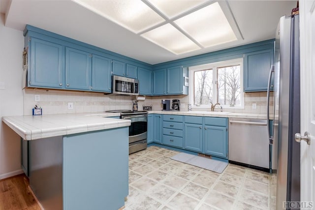 kitchen featuring stainless steel appliances, tile counters, blue cabinets, and sink