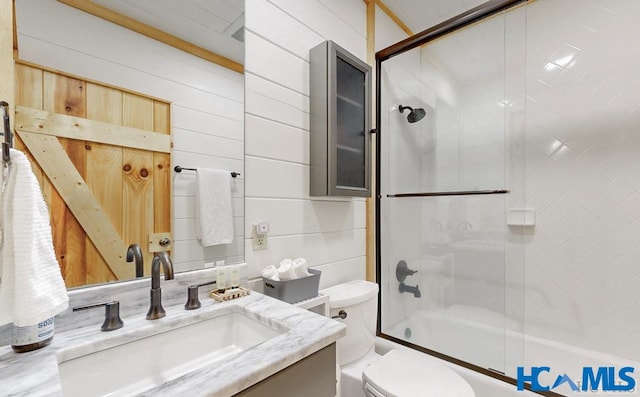 full bath featuring wooden walls, enclosed tub / shower combo, vanity, and toilet