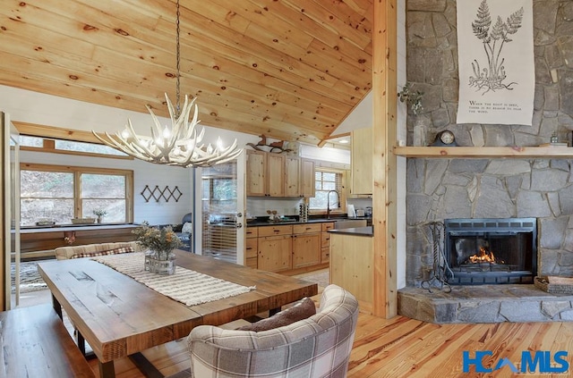 dining space featuring a chandelier, lofted ceiling, a stone fireplace, wood ceiling, and light wood-style floors