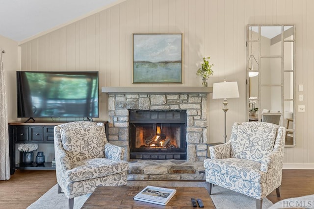 living area featuring wooden walls, a stone fireplace, vaulted ceiling, and hardwood / wood-style floors