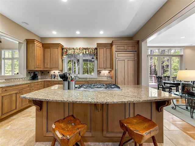 kitchen with stainless steel gas cooktop, backsplash, a wealth of natural light, and a breakfast bar