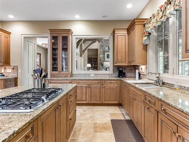 kitchen featuring tasteful backsplash, stainless steel gas cooktop, a sink, light stone counters, and glass insert cabinets