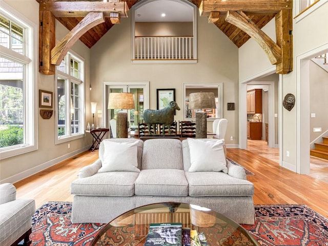 living area featuring stairway, high vaulted ceiling, baseboards, and light wood finished floors